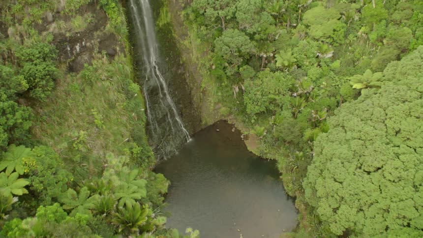 A waterfall in the middle of the forest is being filmed by a drone