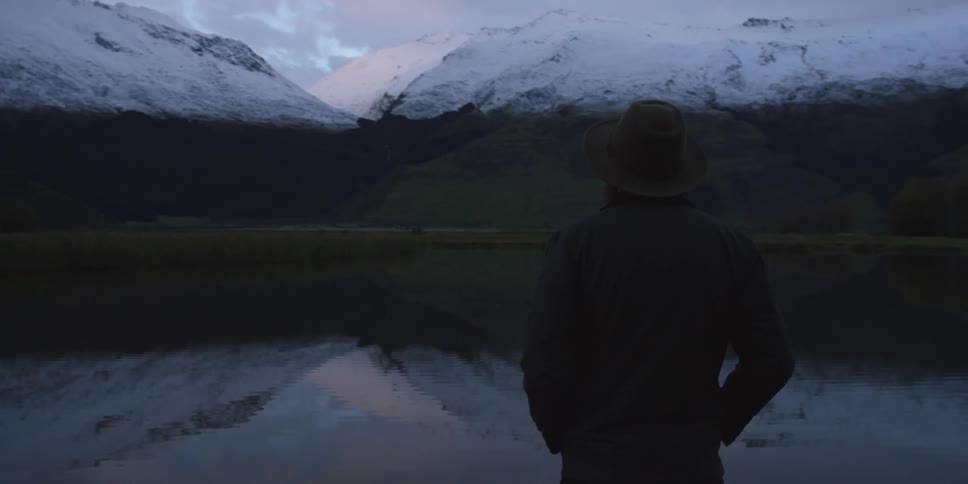 Man stands at the edge of the cliff and looks at the snow covered mountains