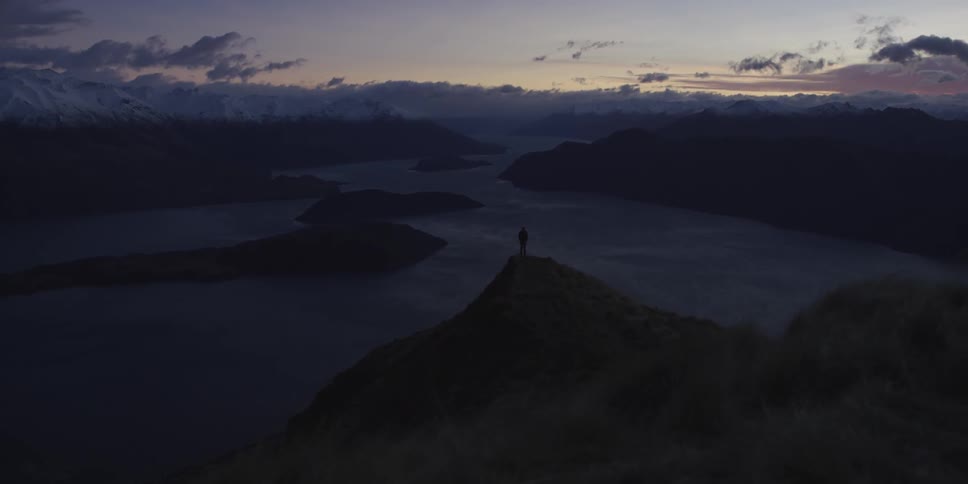 A man stands on a peak overlooking a river