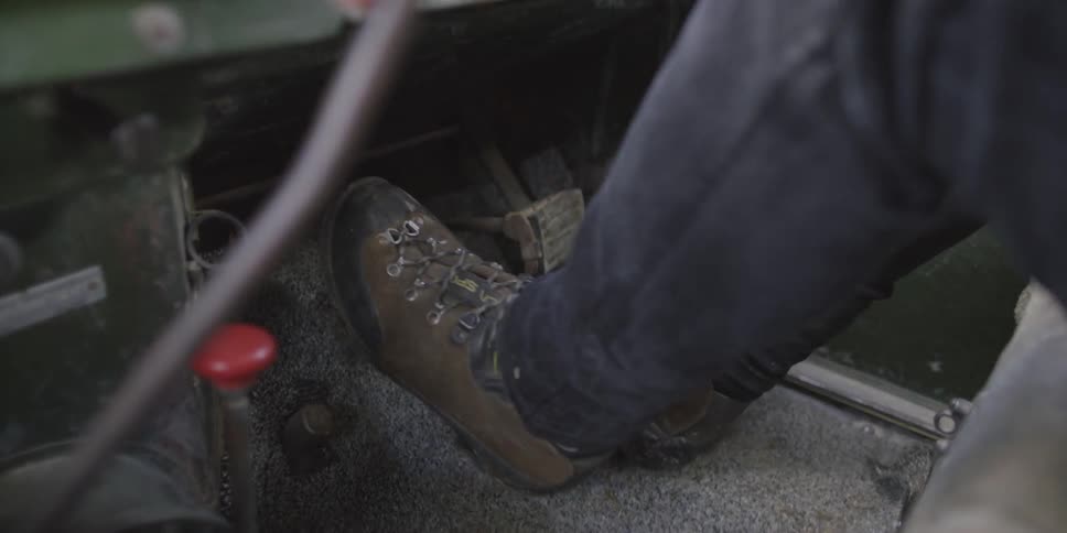 Feet operating pedals and a hand operating the gear shift on the floorboard of a moving tractor
