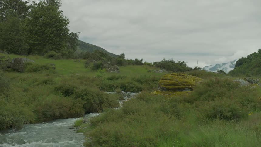 A small stream is being filmed coming from a green field