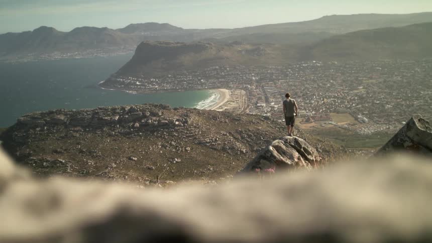 A man is standing on top of a cliff overlooking a beach and town