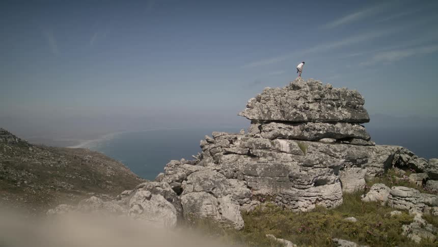 A man climbs up to the top of a rock pillar in a natural setting