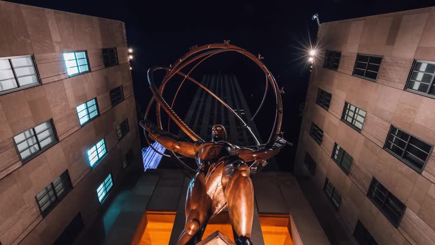 A statue of a man holding up a sphere is filmed from the ground