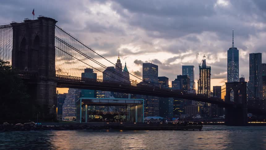 Water flowing under a bridge next to a city on a cloudy day turning into evening