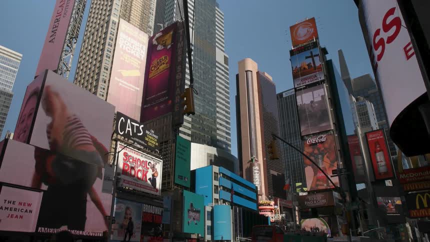 People cross the street as the digital billboards play