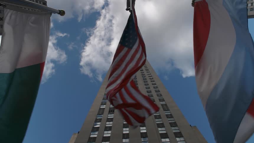 Flags billow in the breeze in front of a skyscraper