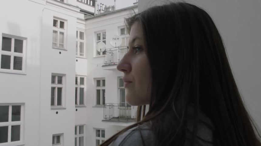 A woman stands out on a balcony and looks around during the day