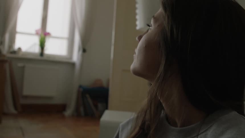 A woman sits in an apartment and looks towards the window