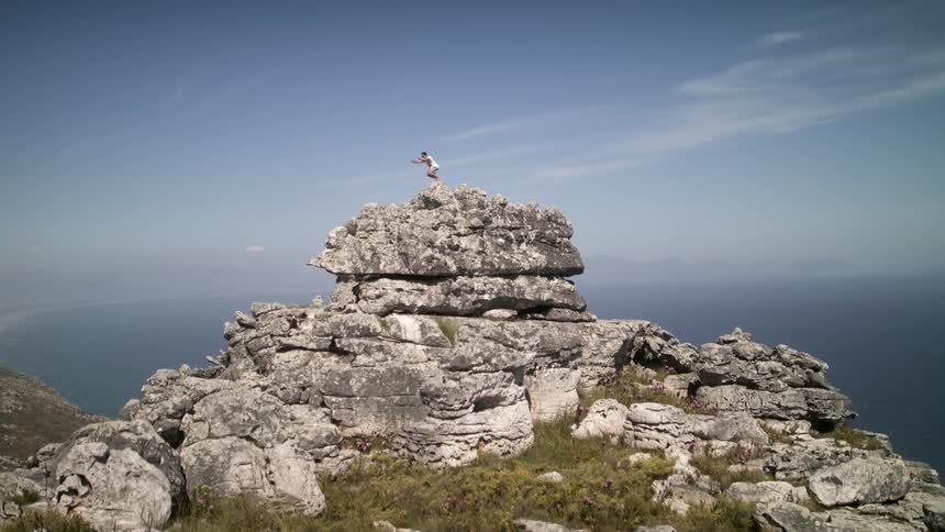 Man jumps on top of a rocky cliff next to the ocean
