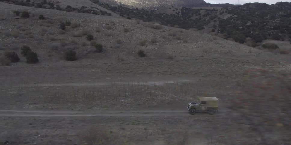 A green jeep drives down a dirt road near mountains