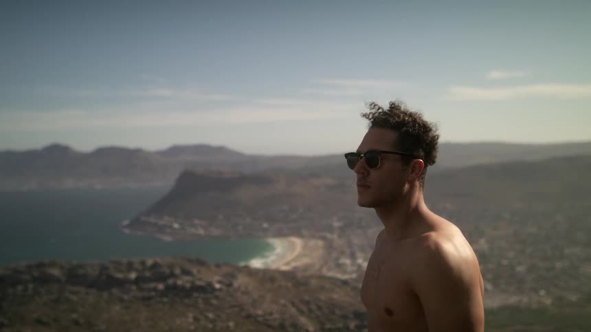 Man stands on a cliff near water on a sunny day