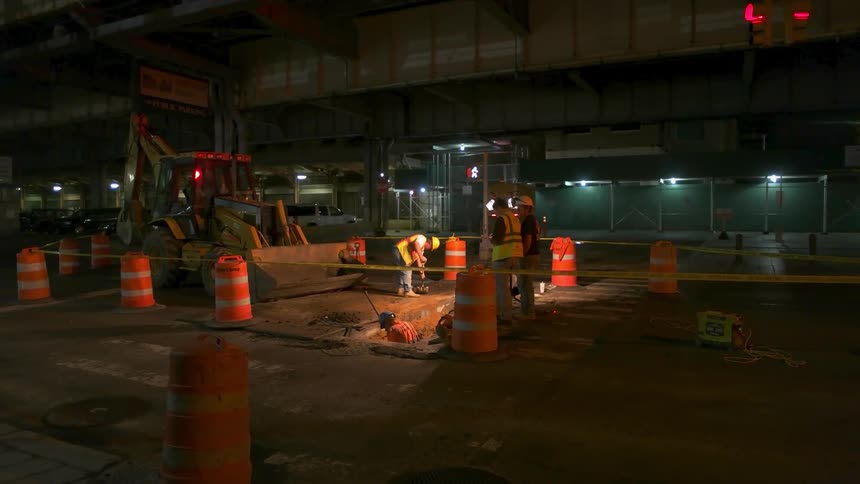 Men dig with shovels at a road construction site at night
