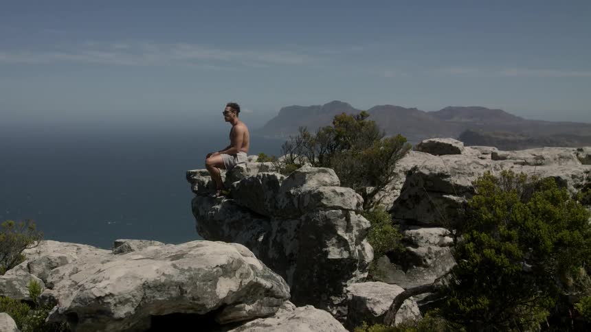 A man is sitting on the cliff of a mountain