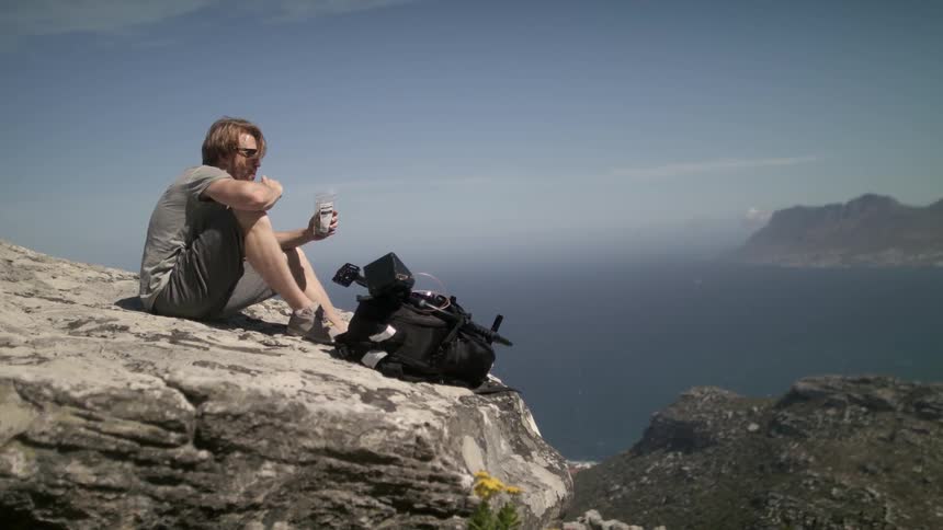 Man eats at the edge of a cliff overlooking water