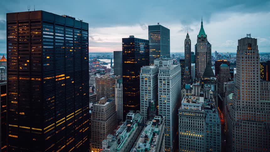 Tall city buildings illuminate the night sky as morning approaches