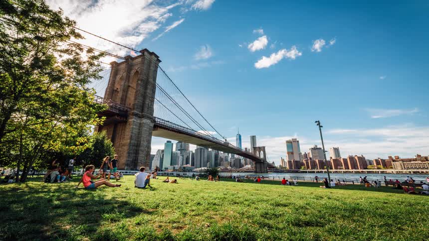 Timelapse of people sitting and walking at a park next to a river and bridge