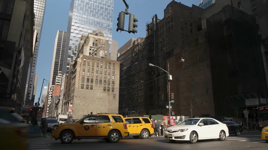 A busy city street is filmed from the sidewalk