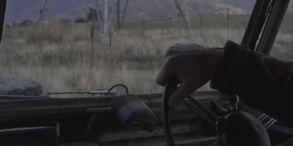 Man drives a vehicle near a field while a truck passes by