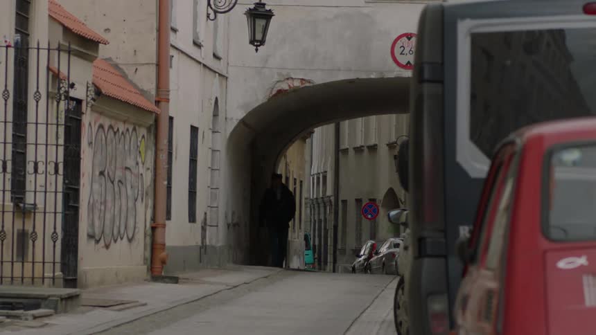 A man walks under an archway on a narrow city street