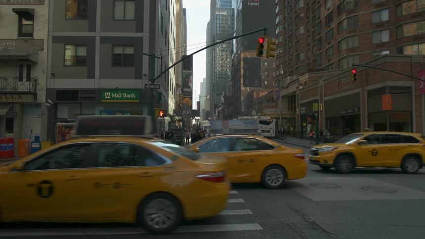 Taxi cabs and vans driving past large buildings in a busy city