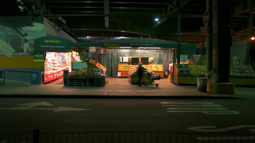 A woman pushes a cart past a street store
