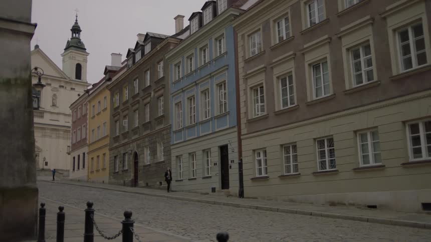 A woman walks down a sidewalk lined with old buildings