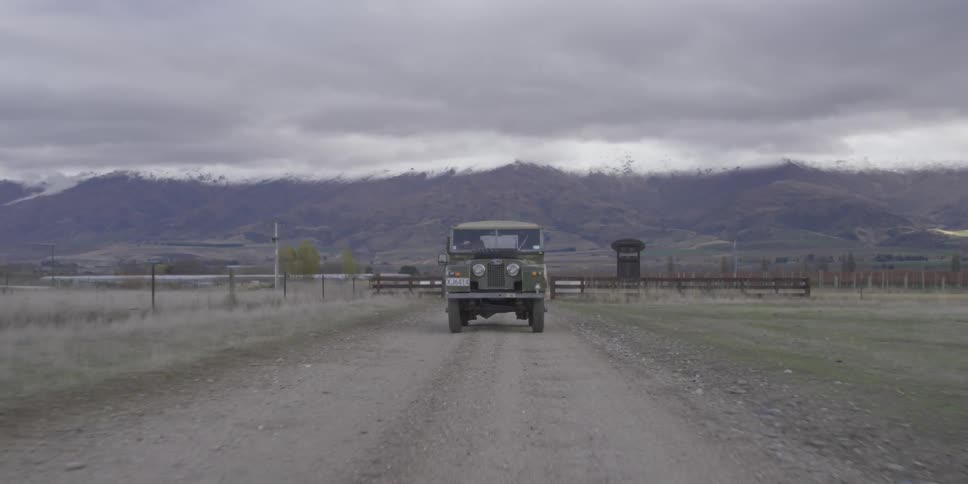 A green jeep drives down a dirt road near mountains