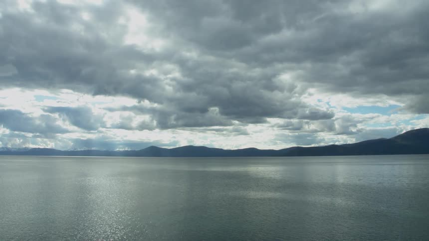 Large body of water rippling before a mountainous area on a cloudy day