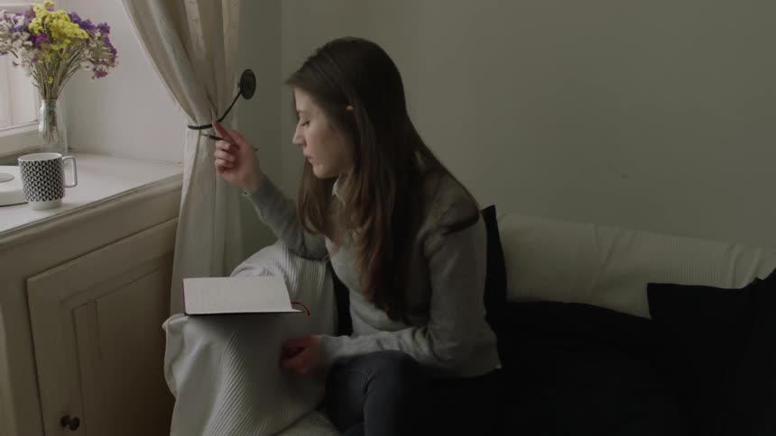 Woman drinks from a mug then writes in a notebook