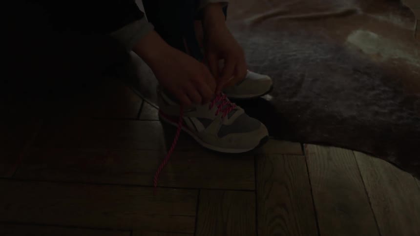 A woman puts on tennis shoes and ties them