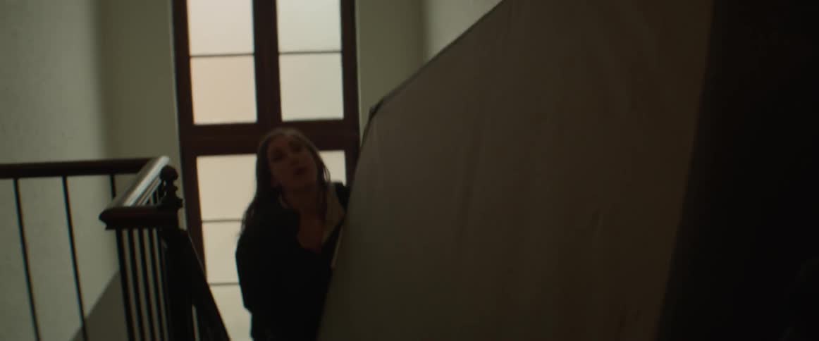 Two women carry a bed up stairs