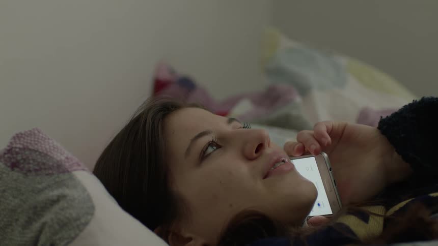 A girl lays in bed and talks on the phone