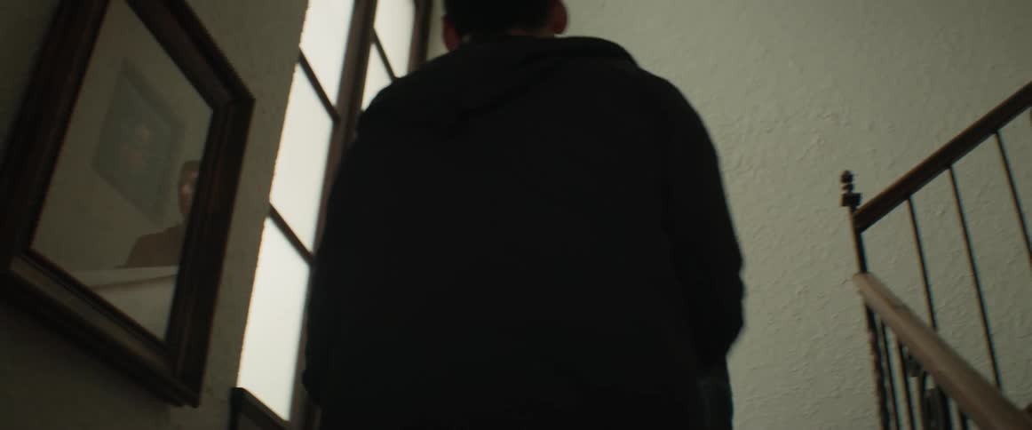 Two men carry a rolled up rug up the stairs