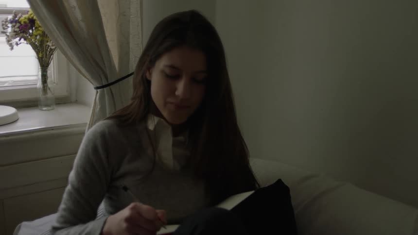 A woman is sitting on a couch writing in a journal