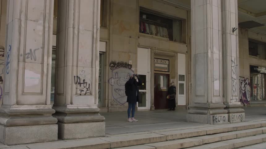A woman standing in front of a building raises her camera to take a photograph