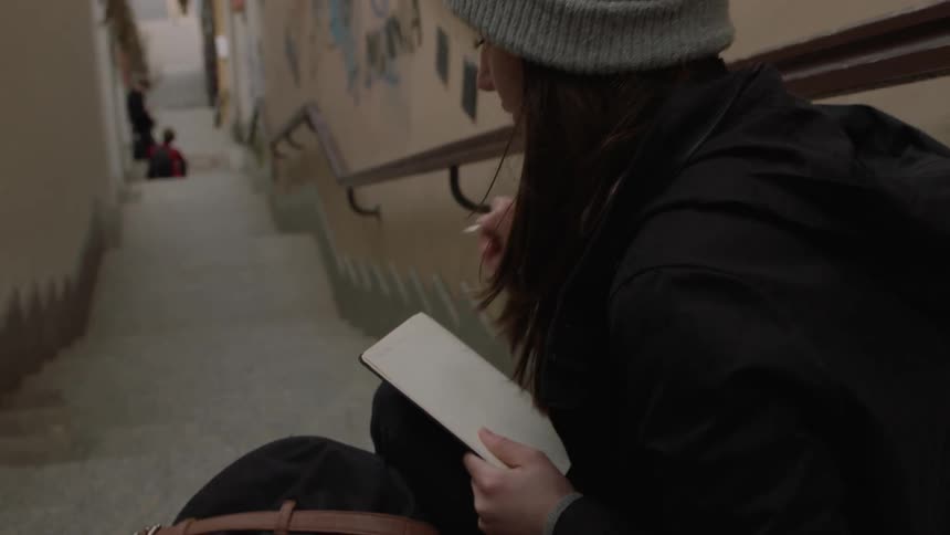 Woman sitting on steps outside writing on a small notepad