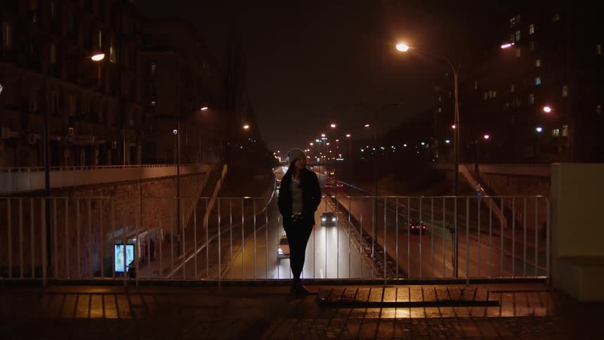 Woman leaning on a railing on a bridge with cars passing underneath