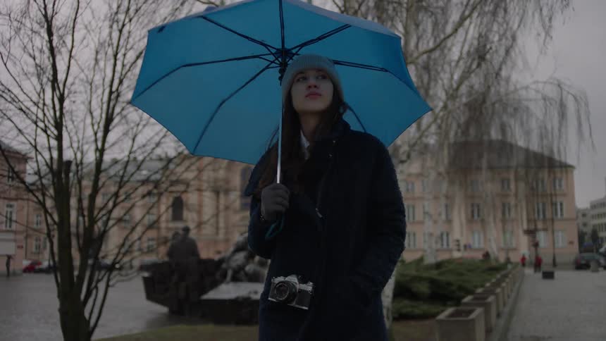 A woman holds a blue umbrella in the rain