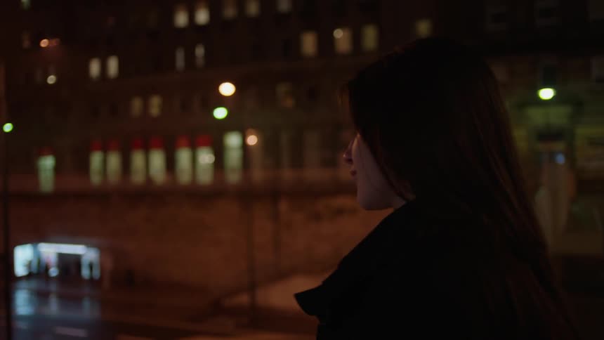 Woman standing on an overpass in a city at night