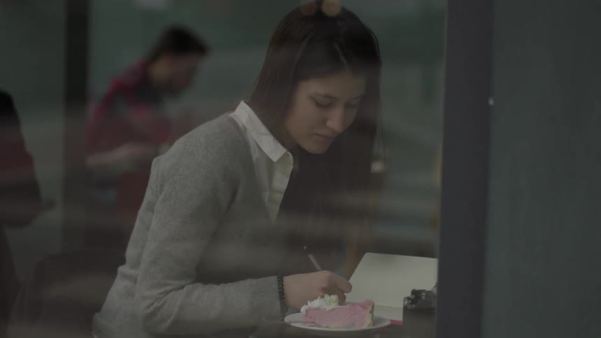 A girl writes in a notebook inside a cafe