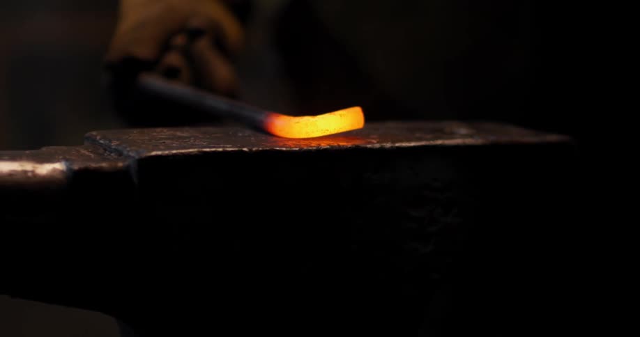 A person uses a hammer to form a hot, metal rod
