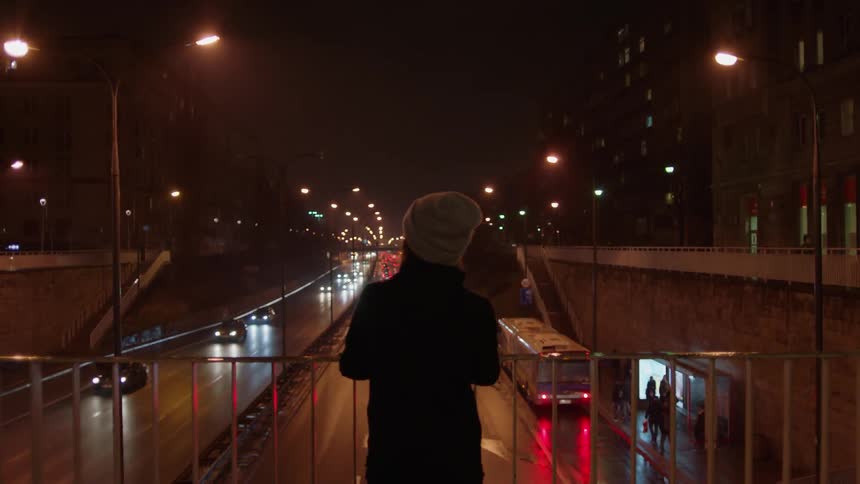 A woman is leaning over a railing on a highway at night