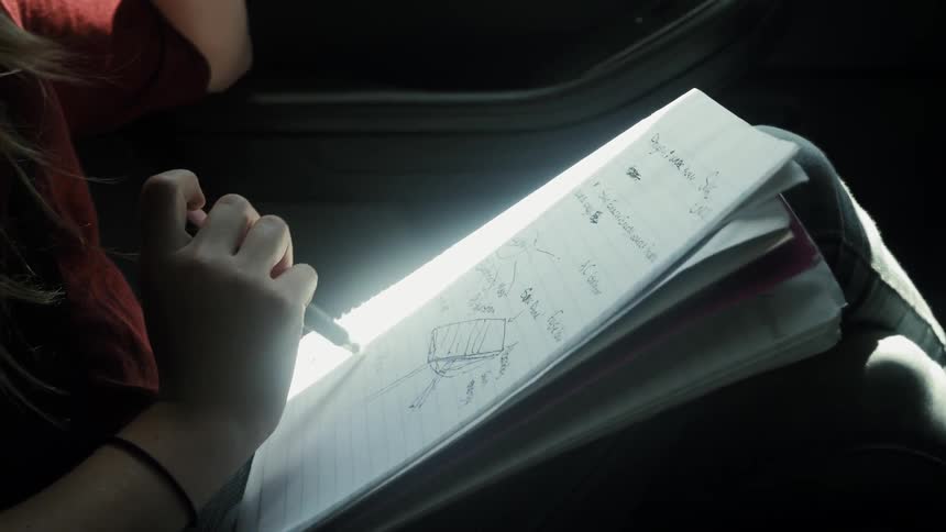 A girl writes in a notebook sitting in a car