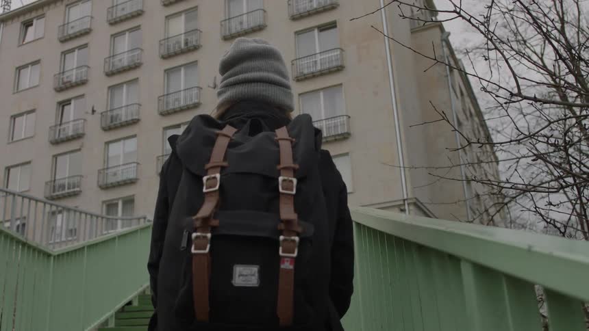 Woman wearing a backpack walks up stairs next to a building