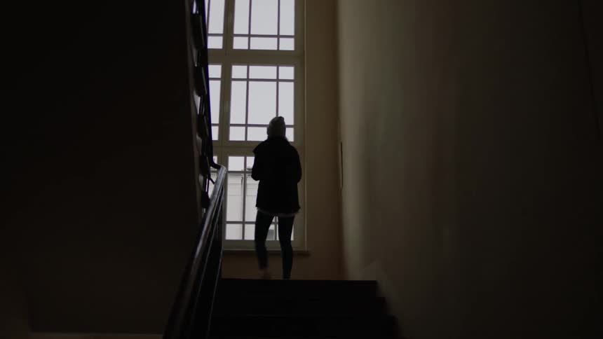 A woman jogs up the stairs and looks out a window