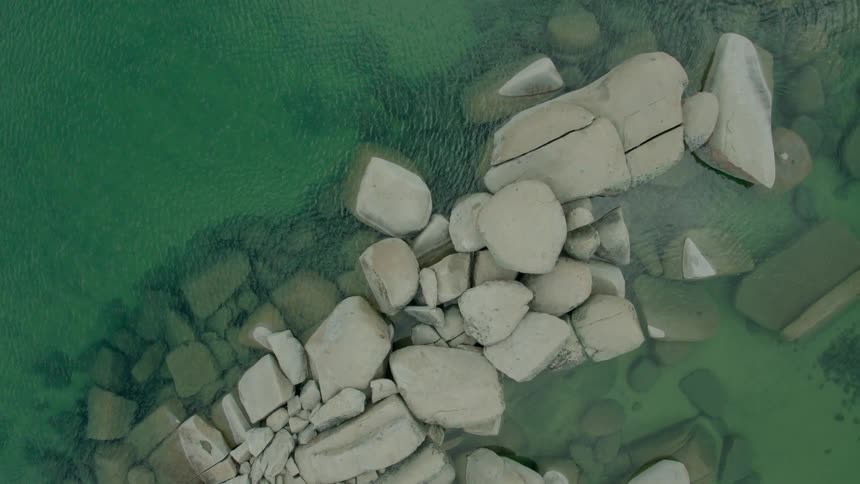 Straight down drone shot that rises to reveal clear blue water around rocks