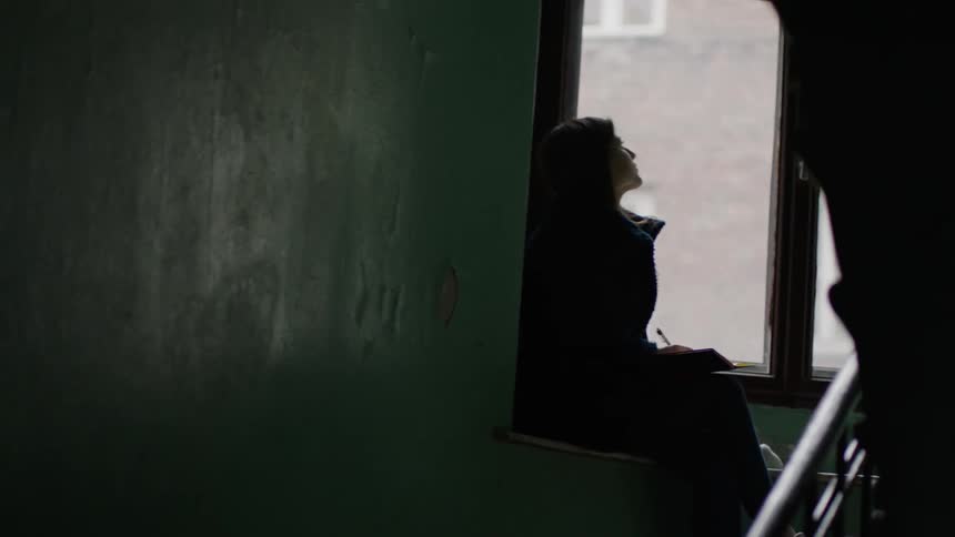 A girl sits on a ledge writing in a notebook
