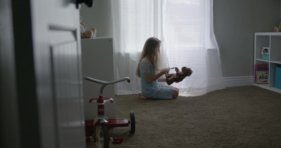 A child plays with her toy bear by the window