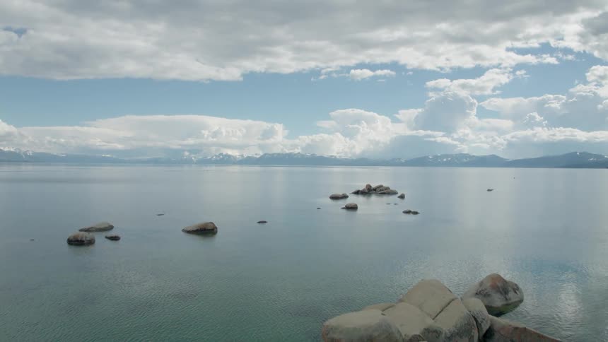 Small rock islands sit in calm expansive water as camera flies over